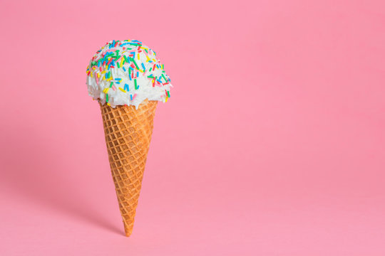 funny creative concept of close up wafer cup with ice cream and colorful sprinkles on pink background, copy space