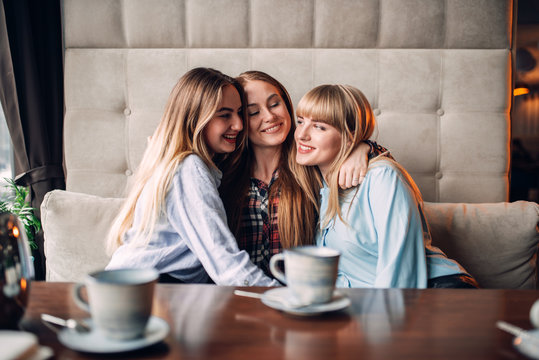 Three attractive girlfriends hugs together in cafe