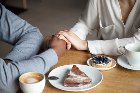 Interracial couple holding hands sit at cafe table, african black man and white woman in love enjoy date in coffee house concept, romantic biracial lovers meet in public place together, close up view - Powered by Adobe