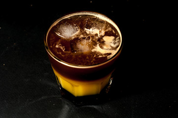 colorful cocktail of bumble or crazy bee with orange juice caramel syrup and espresso coffee in a glass beaker with ice cold summer cocktail on a wooden table coffee machine on the background