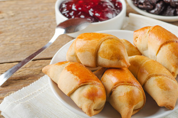 Sweet rolls with prunes on a plate on wooden table with jam and prunes. Homemade sweet pastries.