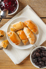Sweet rolls with prunes on plate on wooden table with jam and prunes. Homemade sweet pastries. Top view, flat lay.