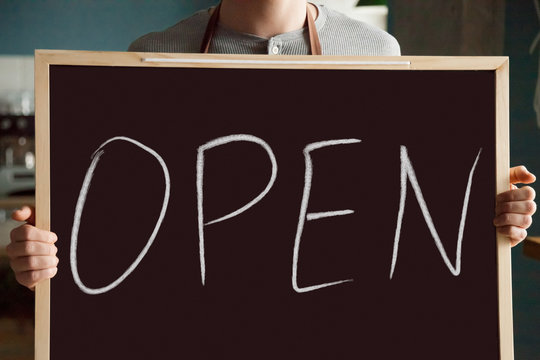 Waiter holding chalkboard inviting visitors to new public place, cafe bar owner advertising coffee shop on first day of work welcoming to cafeteria, open restaurant business concept, close up view