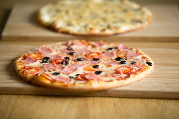 Tasty hot baked pizzas with ham or bacon, tomatoes, olives and cheese on wooden boards on restaurant table, food delivery service for delicious italian meal, pizzeria place concept, close up view