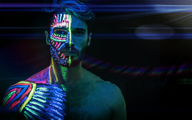 Young man painted in fluorescent paint on face and muscular torso, in studio shot with UV light