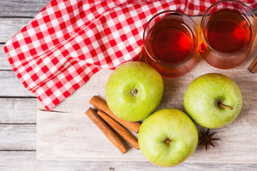 Apple juice in glasses, spices and apples on wooden cutting table 