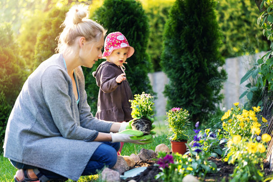 mother and daughter planting flowers together in home garden bed