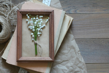 Bouquet of lilies of the valley in a wooden frame on a pile of old books