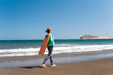 Young sporty girl with surfboard walking along Atlantic ocean coast