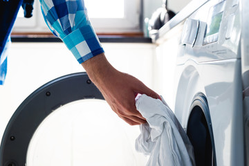 Doing the laundry. Man does the washing in washing machine. Cleaning clothes. Unusual role of a man in role of a woman. Man cares about the house. Father puts clothes in washing machine.