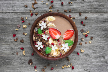 bowl of choclate and banana smoothie with chocolate granola, strawberry and pomegranate seeds decorated with flowers