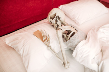 Human skeleton with phone in hand lies in bed