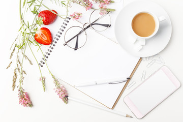 Flowers, notepad, glasses and tea with milk in white cup on a white table. Flatlay. Top view. For design.