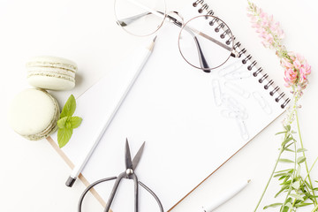 Flowers, notepad, glasses, scissors and cakes on a white table. Flatlay. Top view. For design.