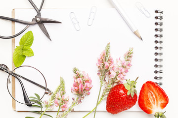 Flowers, notepad, glasses, scissors and strawberry on a white table. Flatlay. Top view. For design.
