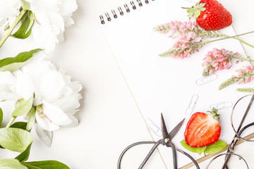 Flowers, notepad, glasses, scissors and strawberry on a white table. Flatlay. Top view. For design.