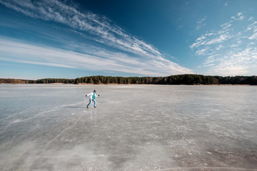 Fototapeta na wymiar Girl in white jacket and blue scarf walking and having fun on ice on the frozen lake in winter