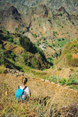 Naklejka na ściany i meble Hiker woman take a rest on mountain slope. Sitting on sharp summit and enjoy spectacular view. Colorful landscape. Bright morning and sunlight in the valley of Coculi on Santo Antao Cape Verde