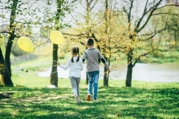 Boy and girl walk with yellow balloons holding hands