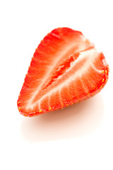 Halve of a strawberry on a reflective white background.