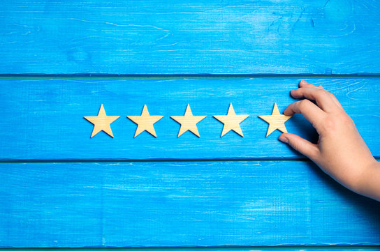 The hand puts the fifth star. The critic determines the rating of the restaurant, hotel, institution. Quality mark. Overview. Five wooden stars on a blue background. A new level of the rating.