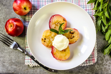 Baked peaches with ice cream on a plate on a gray metal background