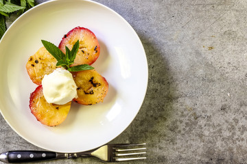 Baked peaches with ice cream on a plate on a gray metal background