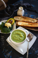 Cream soup of broccoli, avocado and cauliflower with whipped cream on a wooden table. The view from the top.