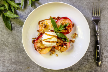 Baked peaches with ice cream on a plate on a gray metal background