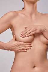 Young topless woman doing breast self-exam (BSE). Checking up breast changes, possible lumps, distortions or swelling.  Breast cancer awareness.