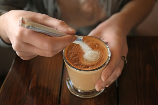 Woman adding sugar to aromatic coffee at wooden table