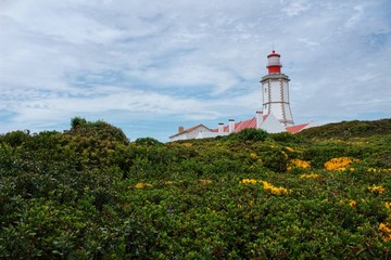 Fototapeta na wymiar Lighthouse on top of cliff and surrounded by vegetation at Cape Espichel