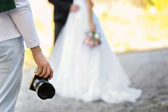 Professional photographer with camera and wedding couple, outdoors