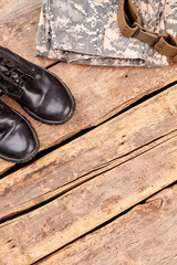 Military leather boots and camouflage clothes. Brown wooden desk background with copyspace.