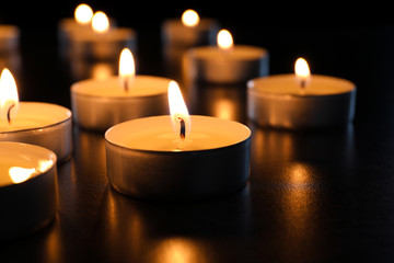 Fototapeta na wymiar Wax candles burning on table in darkness, closeup