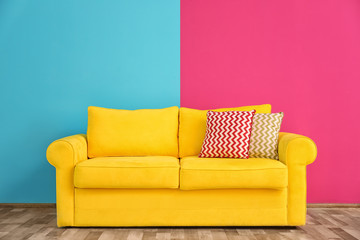 Sofa with different pillows near color wall in room