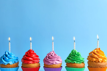 Delicious birthday cupcakes with candles on color background