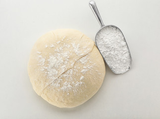 Raw wheat dough and scoop with flour on white background, top view