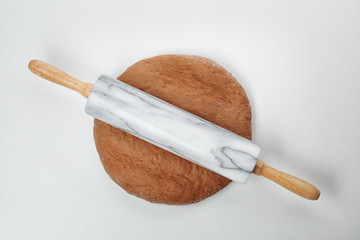 Raw rye dough and rolling pin on white background, top view