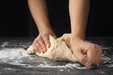 Young woman kneading dough at table, closeup