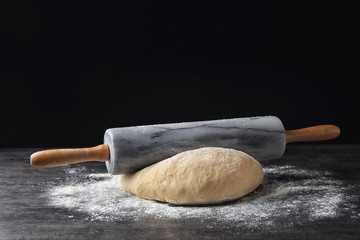 Raw wheat dough with flour and rolling pin on table