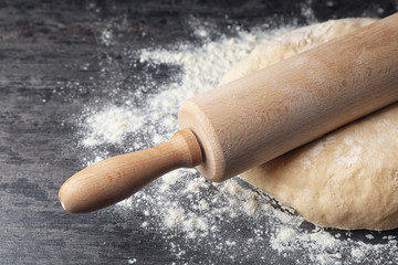 Raw wheat dough with flour and rolling pin on table, closeup