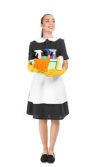 Young chambermaid holding plastic basin with detergents on white background