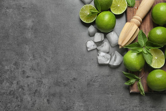 Flat lay composition with ripe limes, ice cubes and juicer on grey background. Refreshing beverage recipe