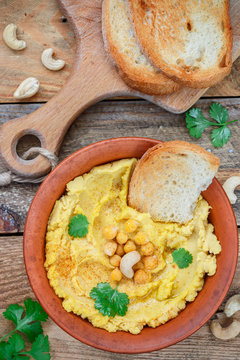Hummus is a traditional middle Eastern snack made of chickpeas with olive oil, garlic and cashew nuts with fresh bread and herbs in a clay plate