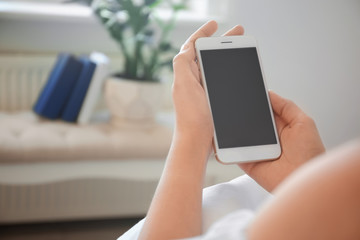 Young woman holding mobile phone with blank screen in hands indoors