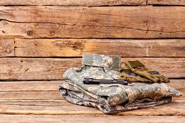 Soldiers camouflage outfit with gloves and flashlight. Wooden desk surface background.