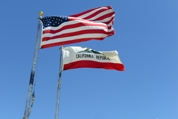 California state flag and American flag with blue sky background, waving in the wind