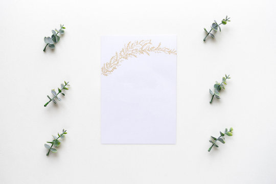 Wedding invitation card and oregano branches on white marble. Top view.