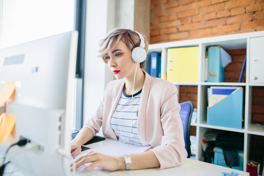 closeup portrait of beautiful stylish web-designer wearing white headphones and using the computer